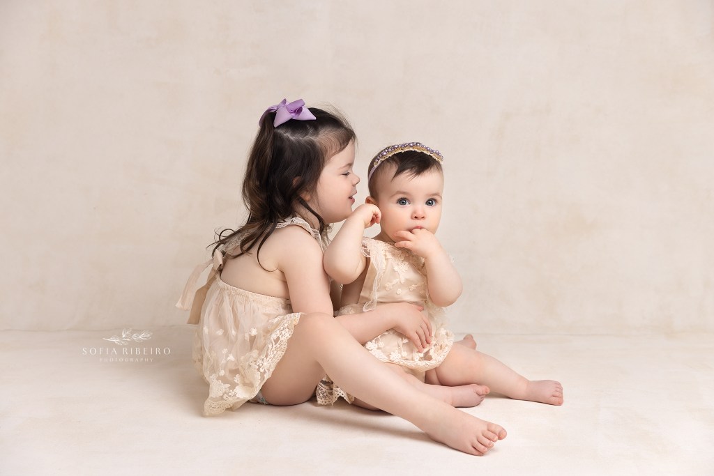 sisters pose in matching cream rompers during a baby session in westfield nj