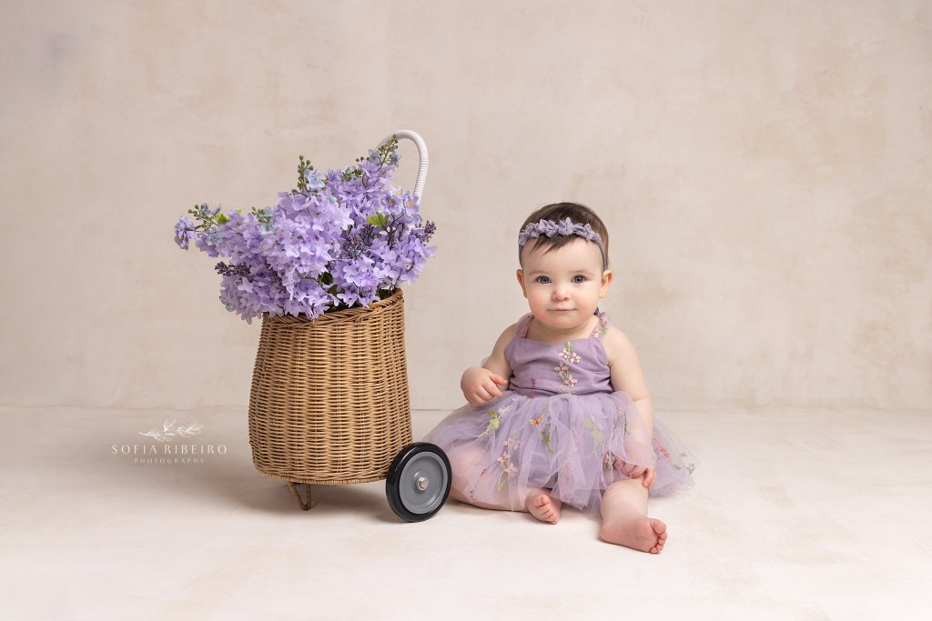 1 year old baby in lavender dress poses with a floral basket