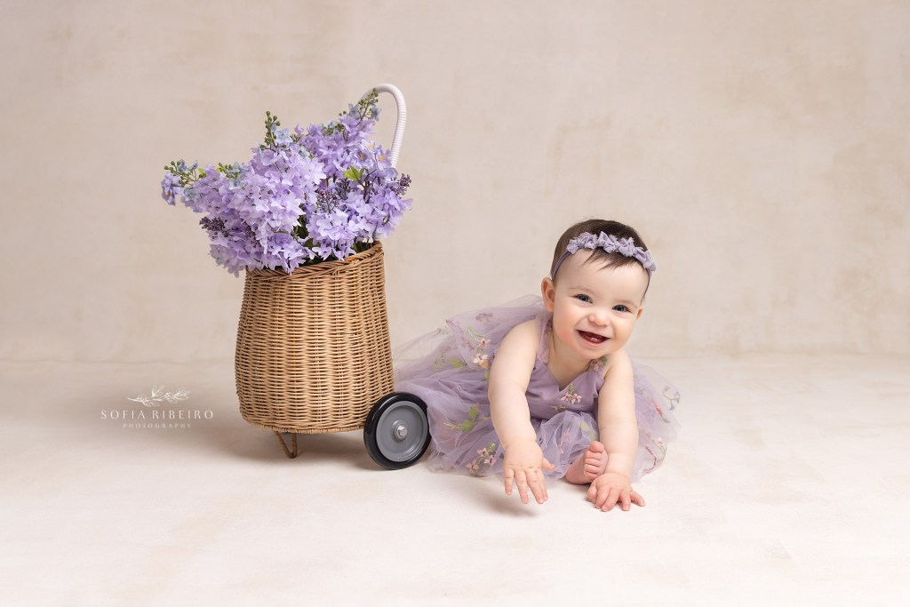 1 year old baby in lavender dress poses with a floral basket