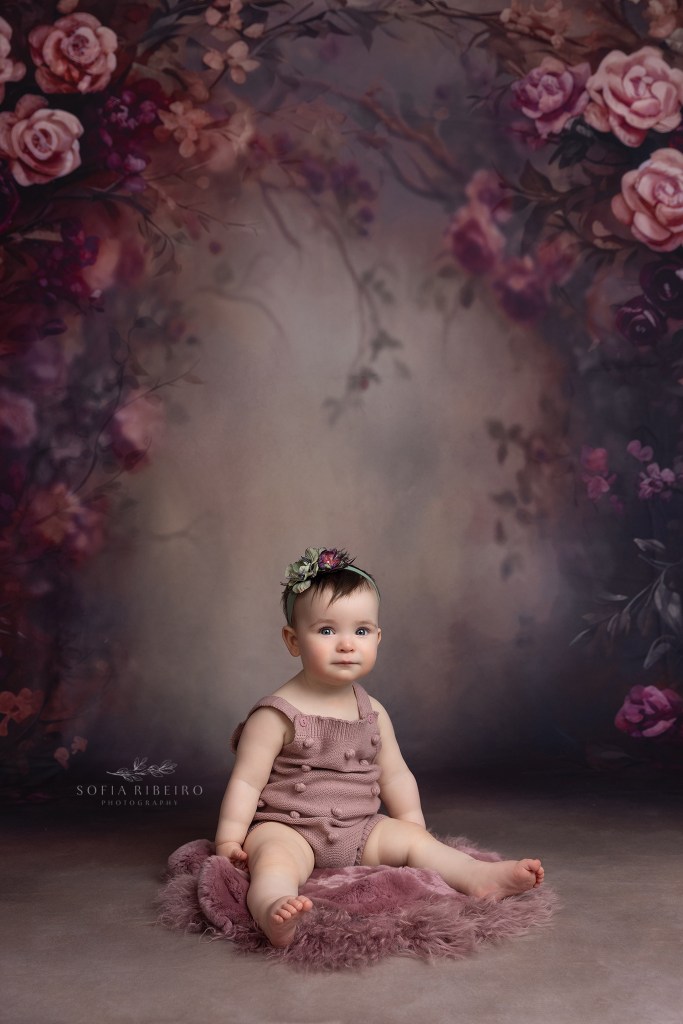 baby girl sits against a floral backdrop during a aby portrait session