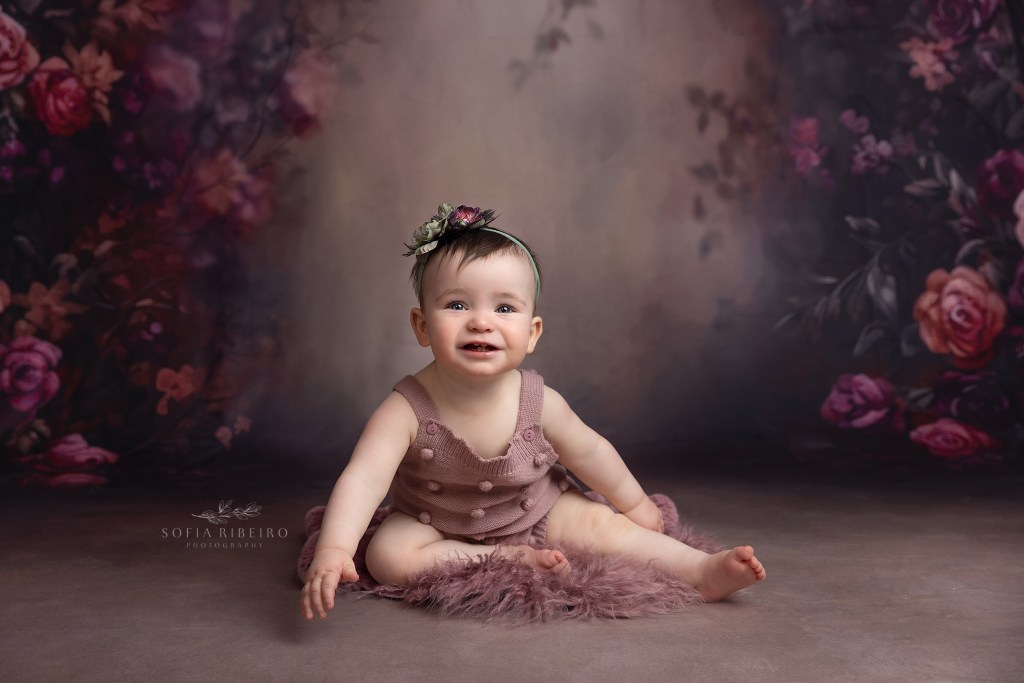 baby girl sits against a floral backdrop during a baby portrait session