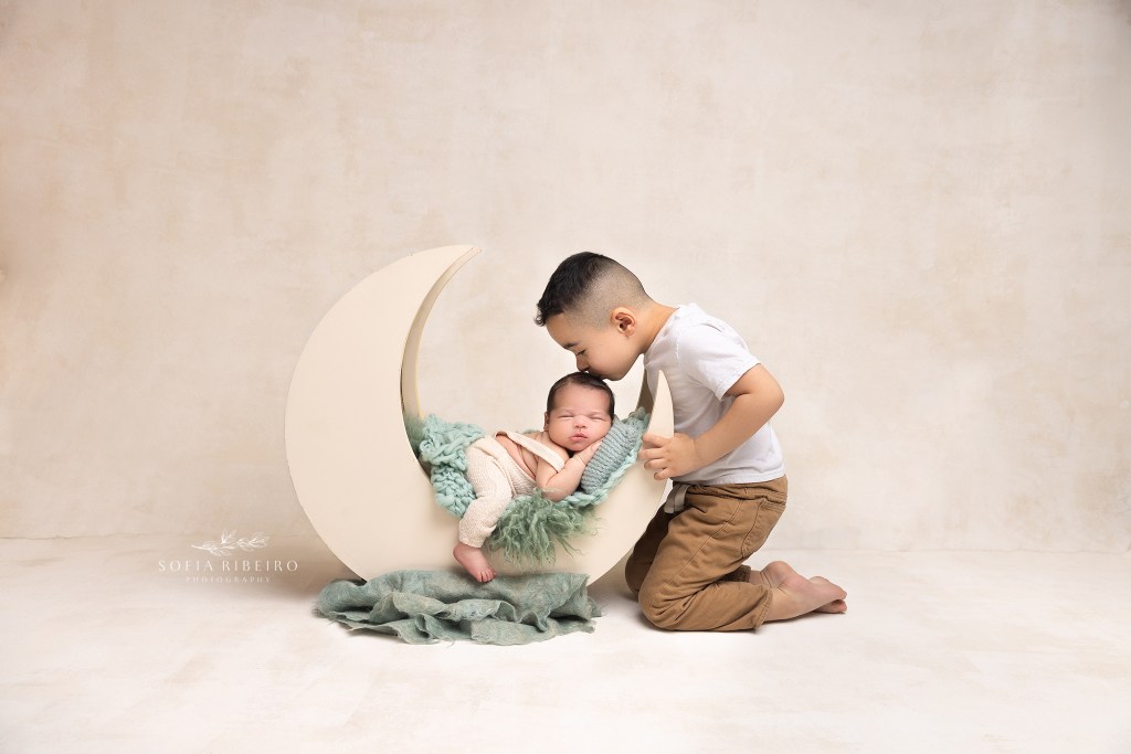 big brother kisses his baby brother on the head while posed on a moon prop