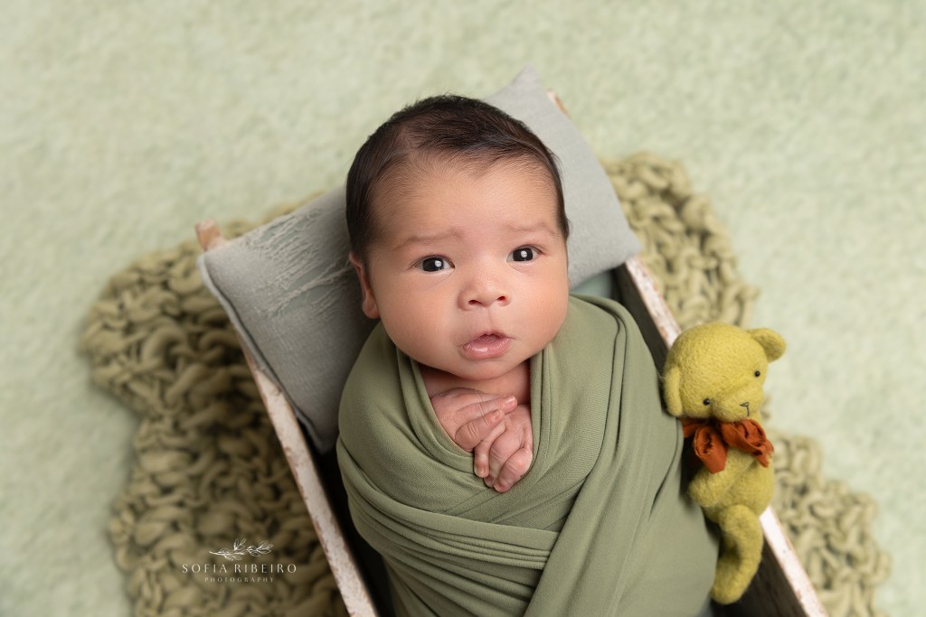 baby boy is snuggled in a green wrap in a tiny crate during a newborn session in wharton nj