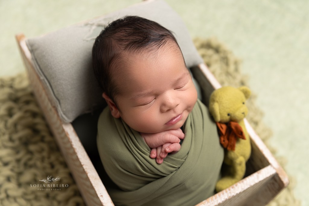 baby boy is snuggled in a green wrap in a tiny crate during a newborn session in wharton nj