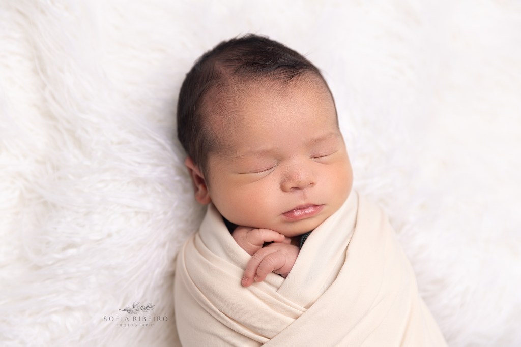 baby boy is snuggled sweetly in a cream wrap during a newborn photo session in wharton nj