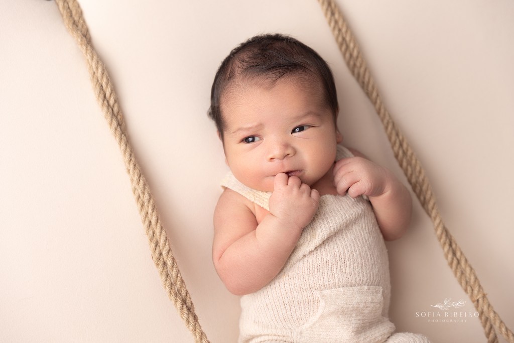 newborn boy "swings" on a prop during a photo session