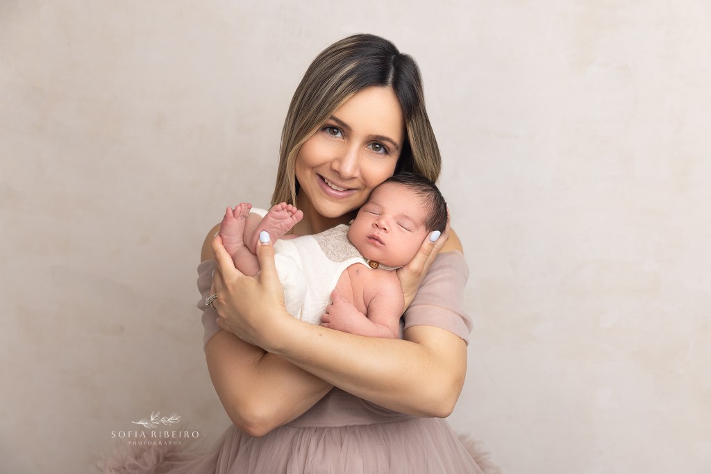 mom smiles at the camera while holding her newborn baby boy
