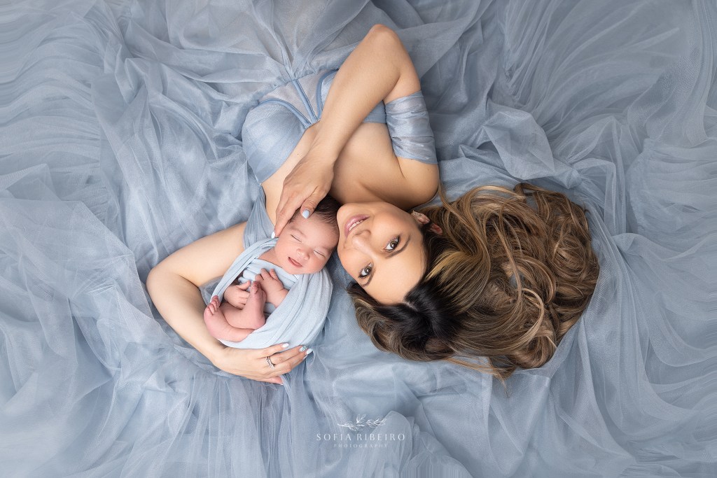 mom smiles surrounded by her babies during a photo session for her newborn