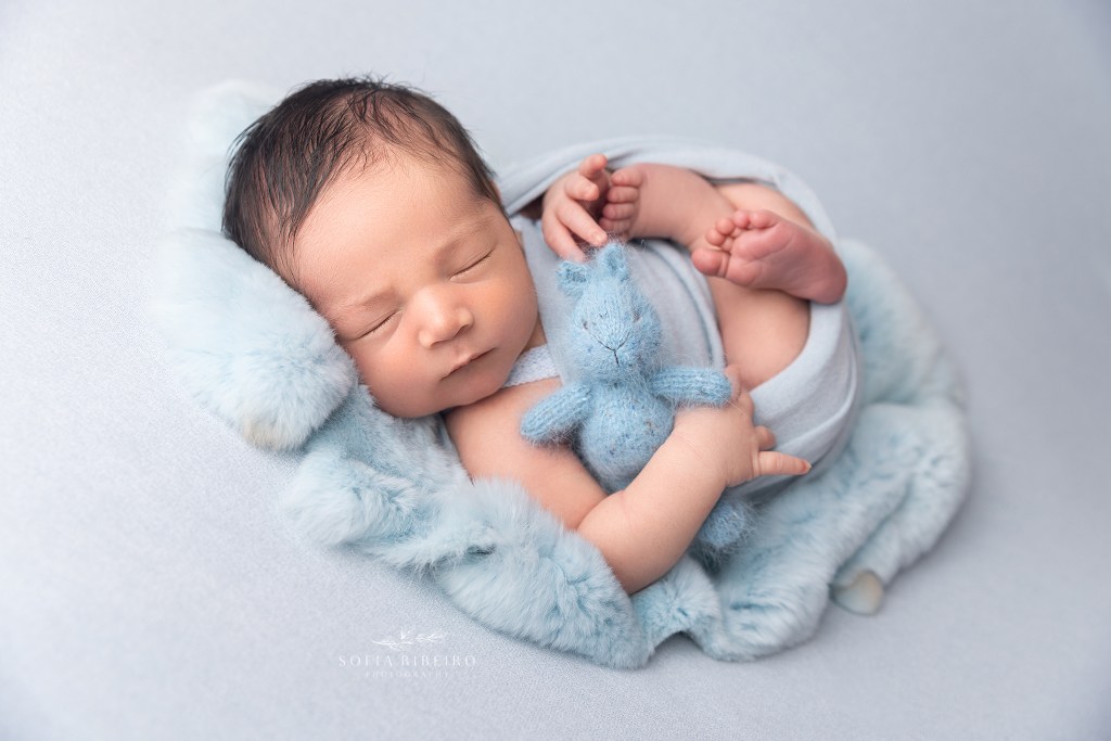 baby is wrapped in a blue wrap snuggling a stuffed bunny