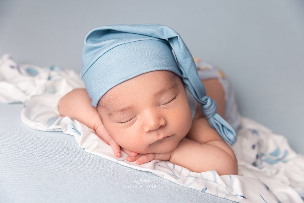 baby boy in a blue sleepy cap nestled on his hands for a photo