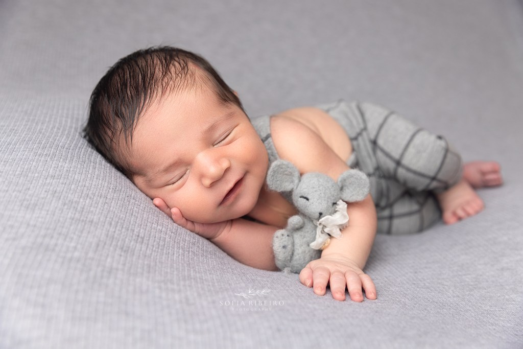 baby smiles in grey overalls with a stuffed bunny during a photo session with a clark nj newborn photographer