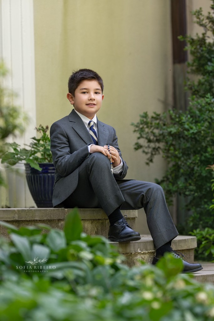 boy poses on stairs in his communion suit during a photo session
