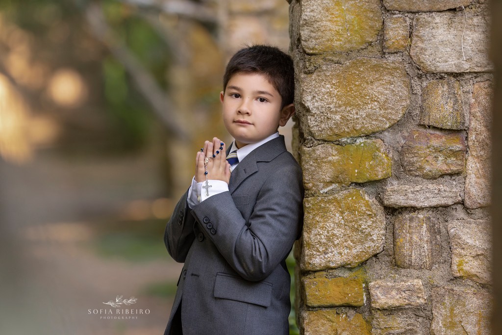 boy poses with rosary in hands against a stone wall for communion portraits in morristown nj