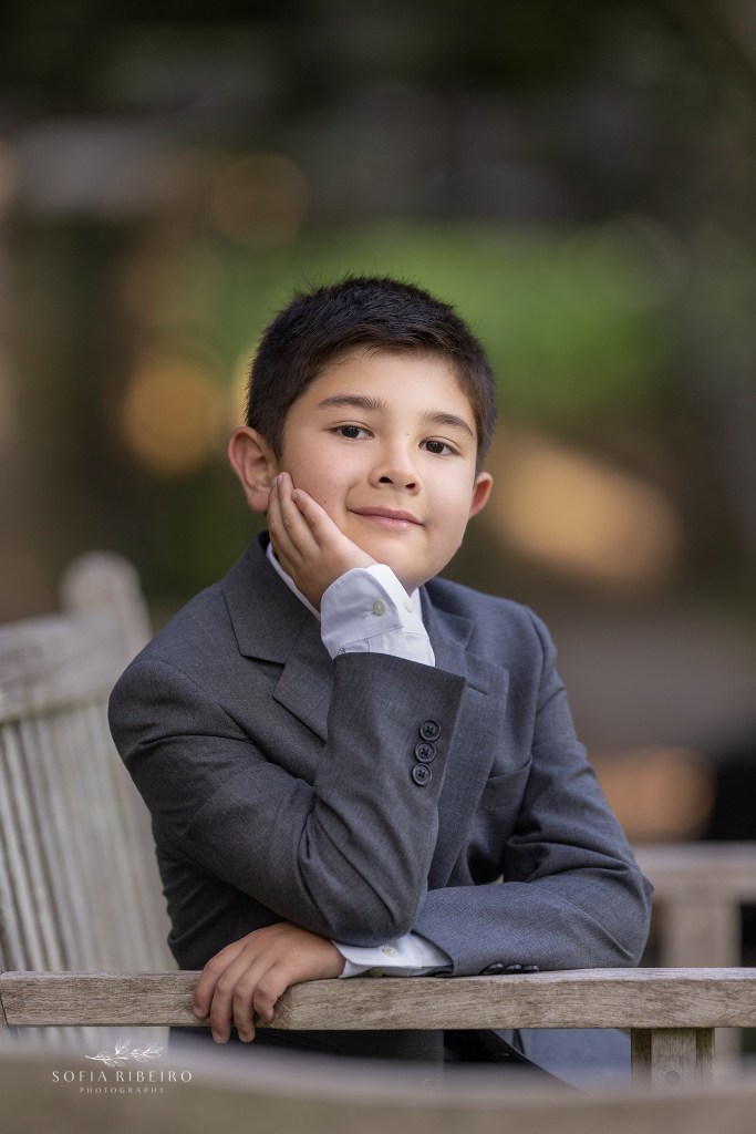 communion photos of a little boy celebrating his first holy communion, posed on a park bench