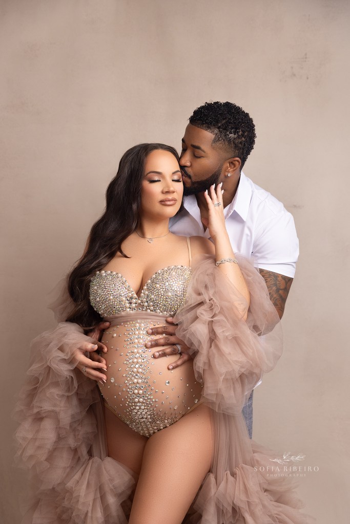 mom poses in a tulle robe and bedazzled bodysuit with dad in a loving embrace for maternity photos in edison nj