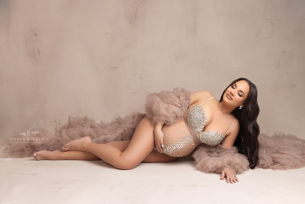 mom poses in a sparkly bodysuit on the floor showcasing her pregnancy belly during a maternity photo session in edison nj