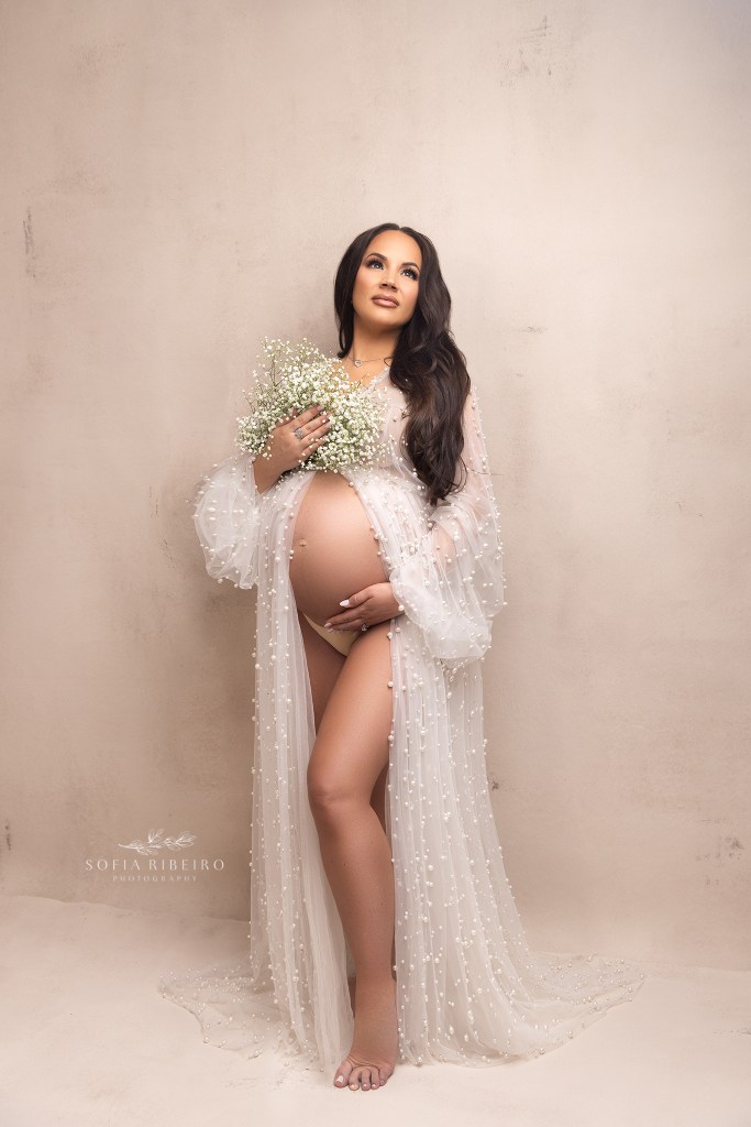 mom cradles her baby bump gently during a maternity session, dressed in a pearl robe