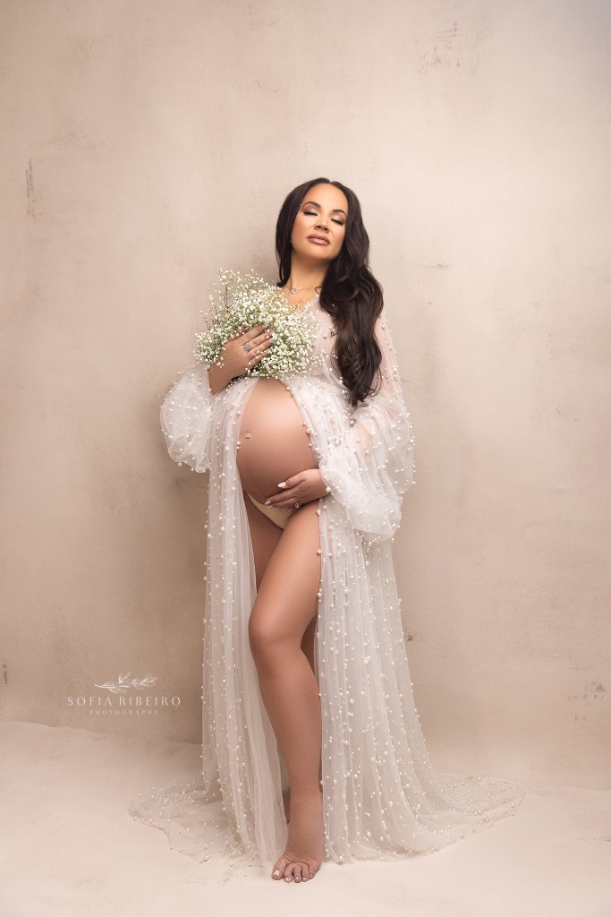 mom cradles her baby bump gently during a maternity session, dressed in a pearl robe