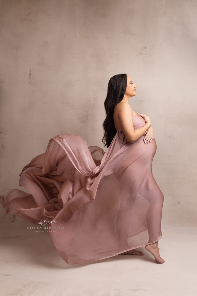 mom is draped in flowing fabric, during a serence moment during a maternity photo session