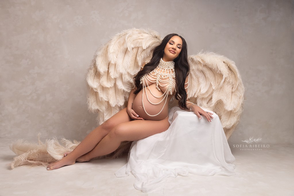 mom to be poses in angel wings and pearls, to celebrate her growing baby bump with an edison nj maternity photographer