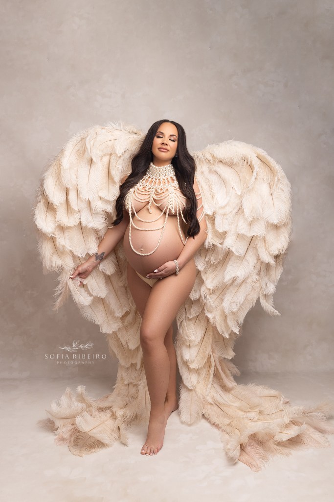 mom to be poses in angel wings and pearls, to celebrate her growing baby bump
