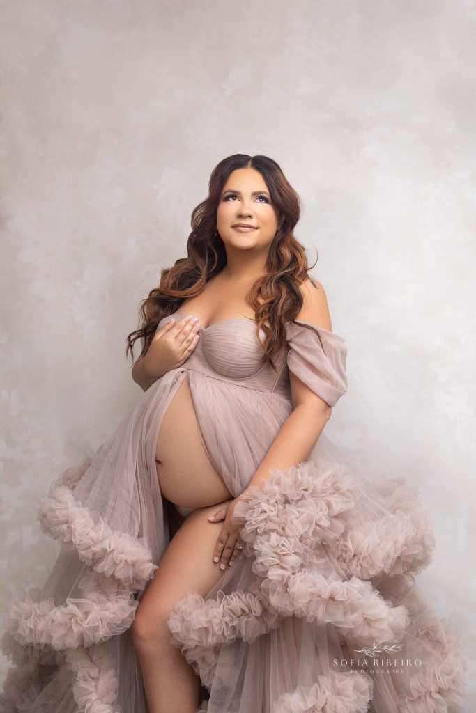 mom poses in a fluffy tulle gown with her pregnant belly exposed during a maternity session