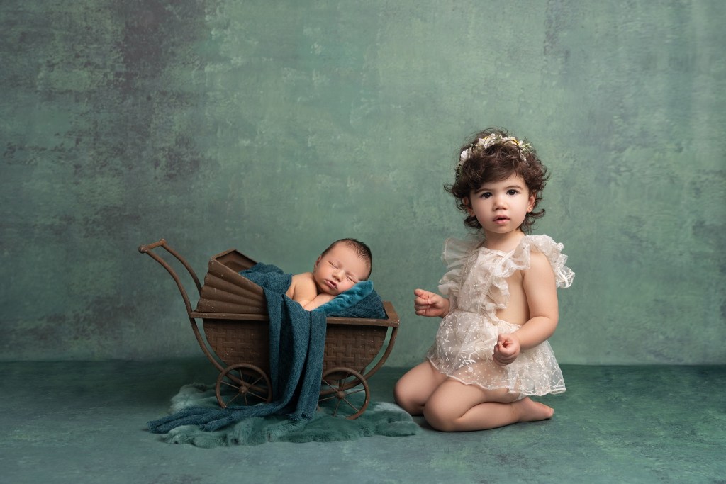 big sister snuggles close to her baby brother in a newborn carriage prop during his newborn photos