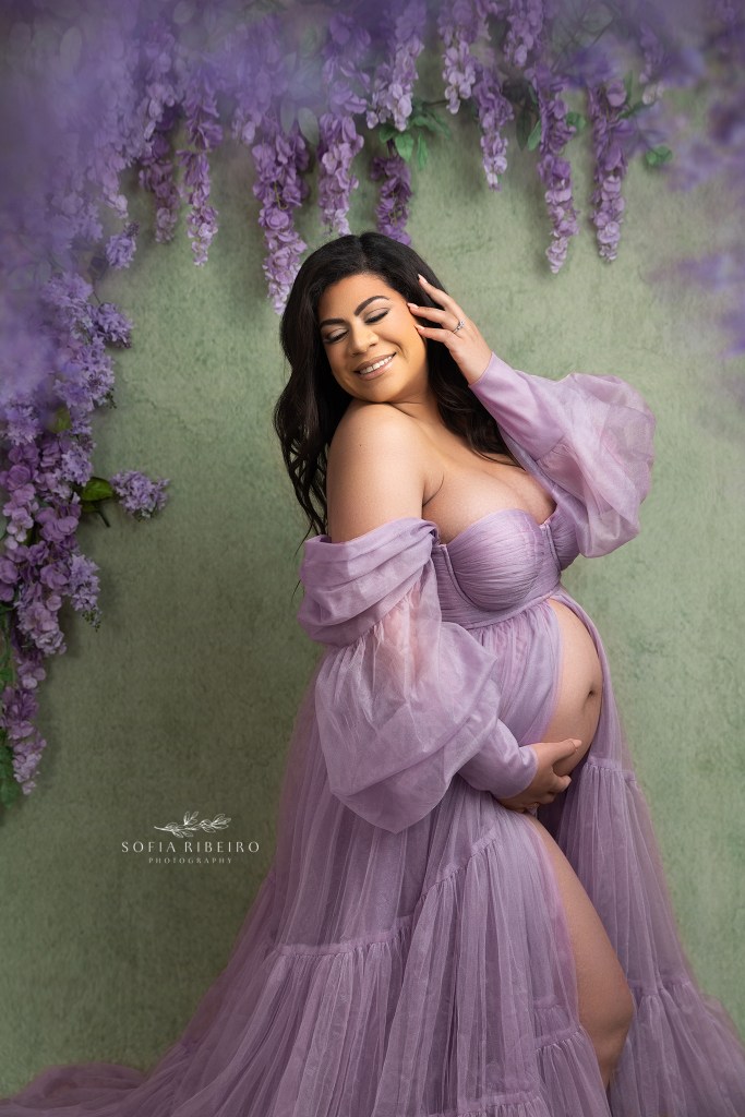 mom smiles while cradling belly in a purple tulle gown during a session with a ridgefield nj maternity photographer
