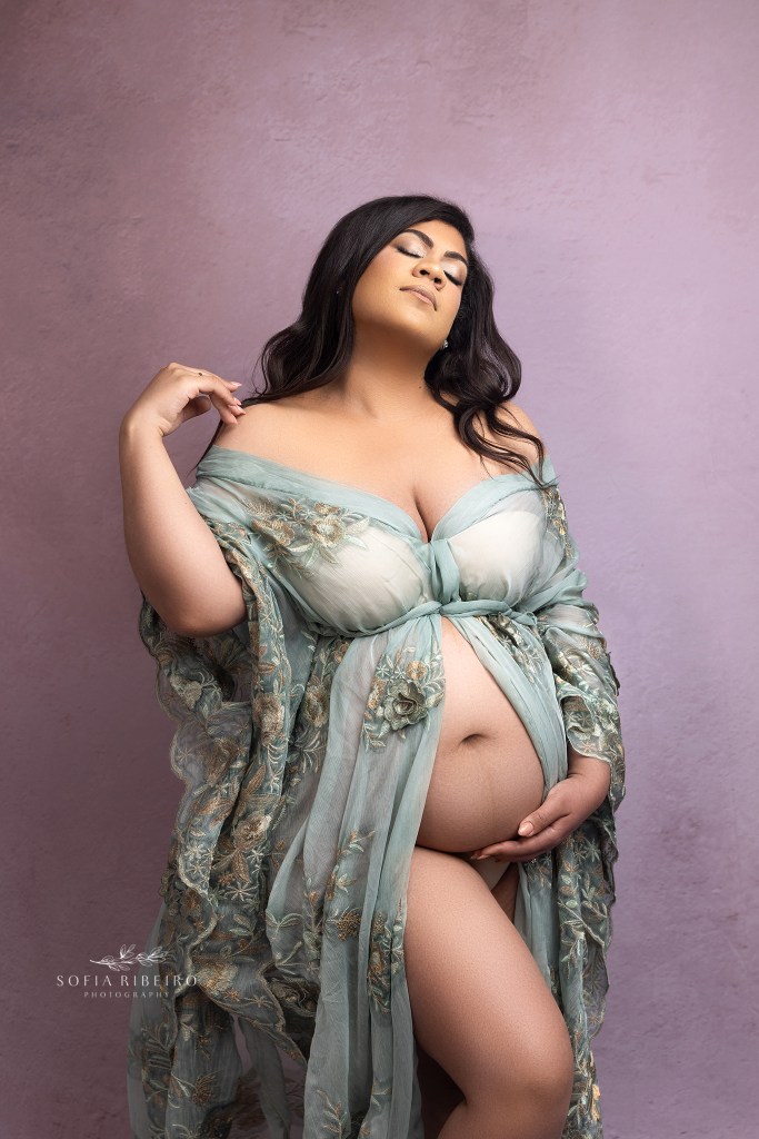 radian mom holds a sage embroidered robe open with her belly exposed against a pink background for maternity photos with a ridgefield nj maternity photographer