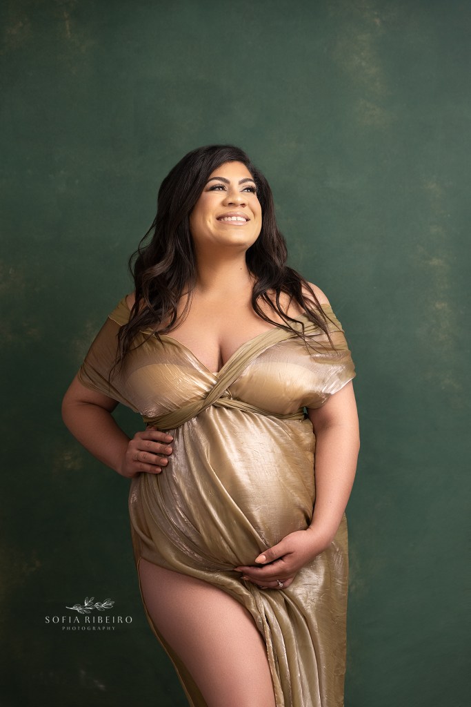 mom to be is a golden goddess in a shimmery gold fabric draped to enhance her growing baby bump
