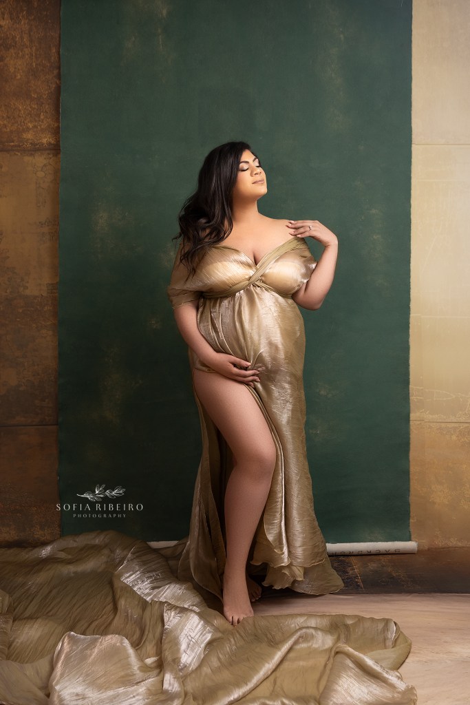 mom to be is a golden goddess in a shimmery gold fabric draped to enhance her growing baby bump
