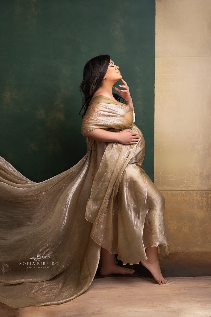 mom poses in a profile, full body pose against a green and gold backdrop for maternity photos in ridgefield nj