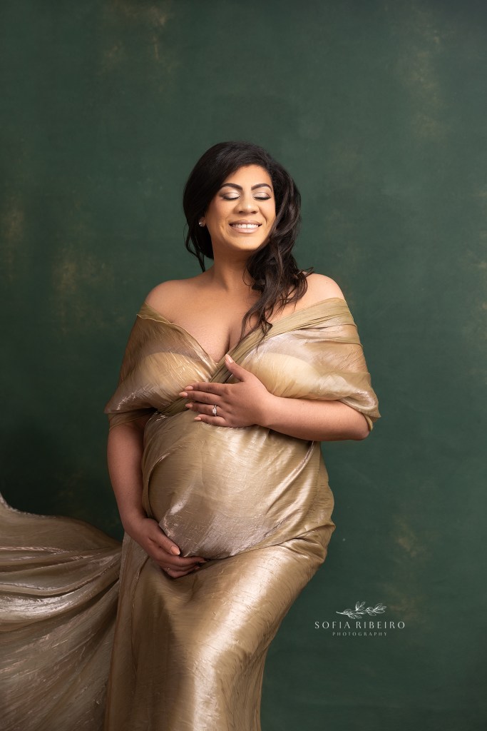 mom to be is a golden goddess in a shimmery gold fabric draped to enhance her growing baby bump