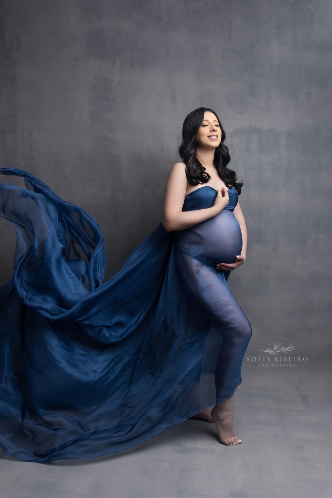mom smiles as she showcases her bump in flowing blue silk with a south amboy nj maternity photographer