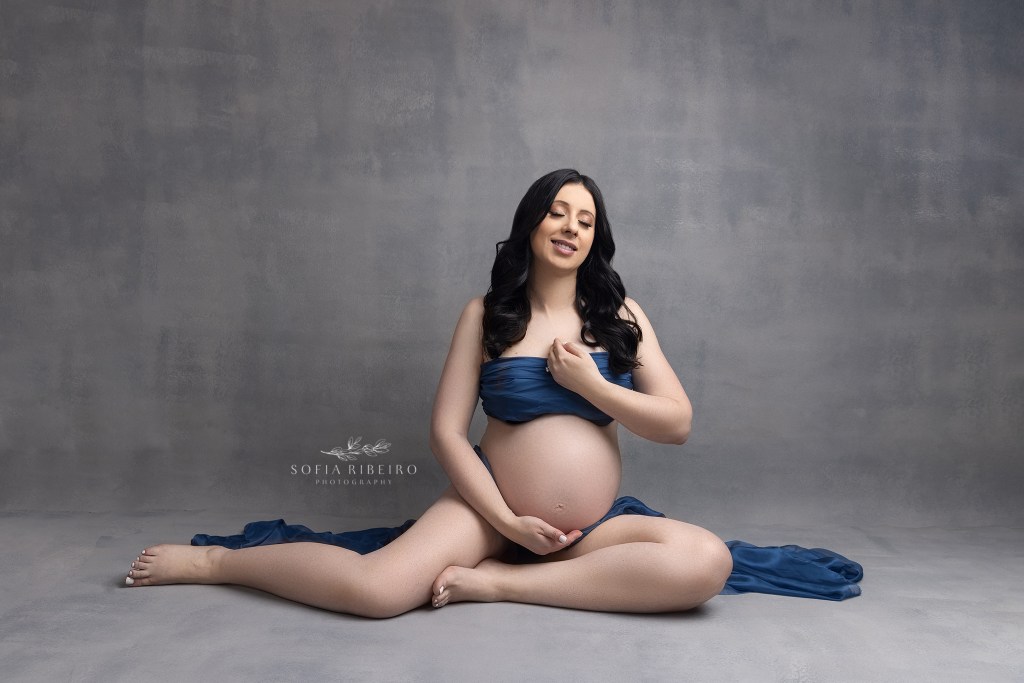 mom is draped in blue fabric, showcasing her baby bump and smiling to herself