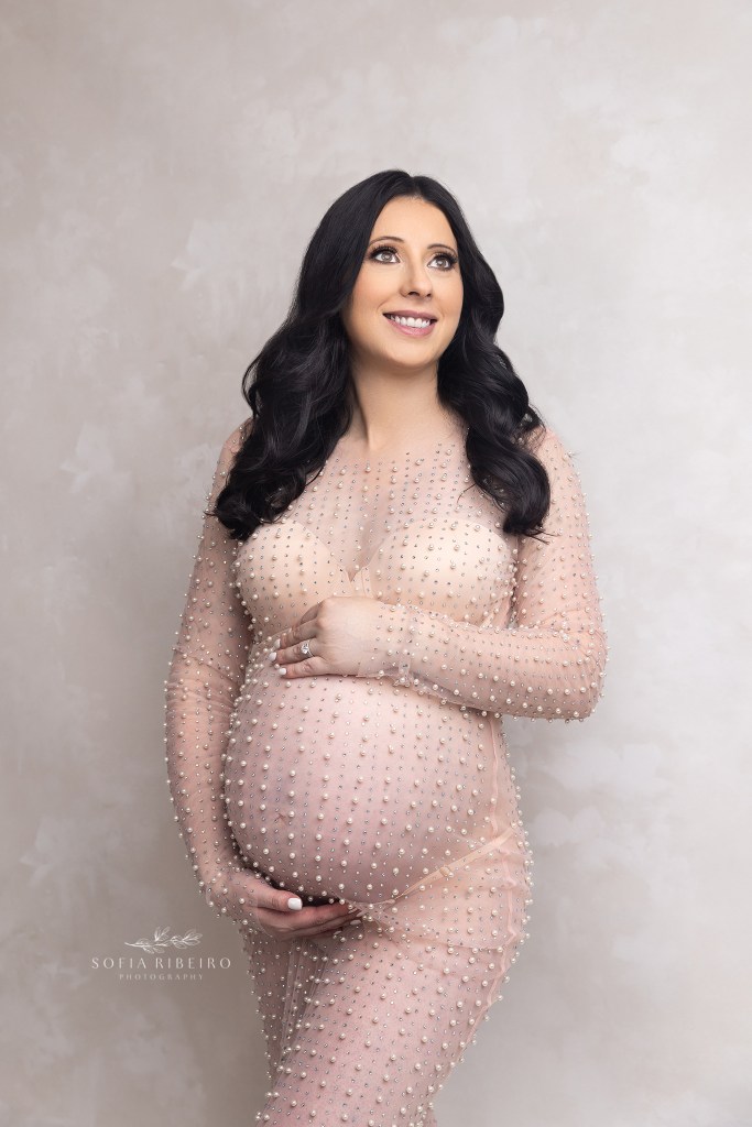 mom poses in a pearl dress hugging her belly during a photography session