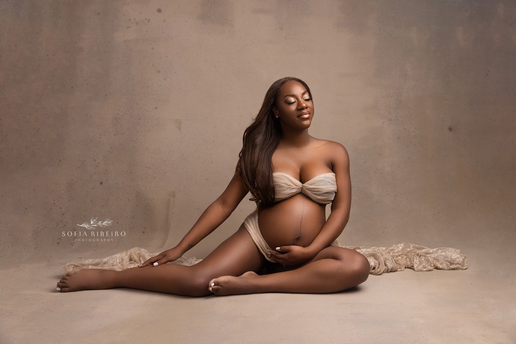 mom poses on the floor draped in gold shimmery fabric during her maternity session in new jersey