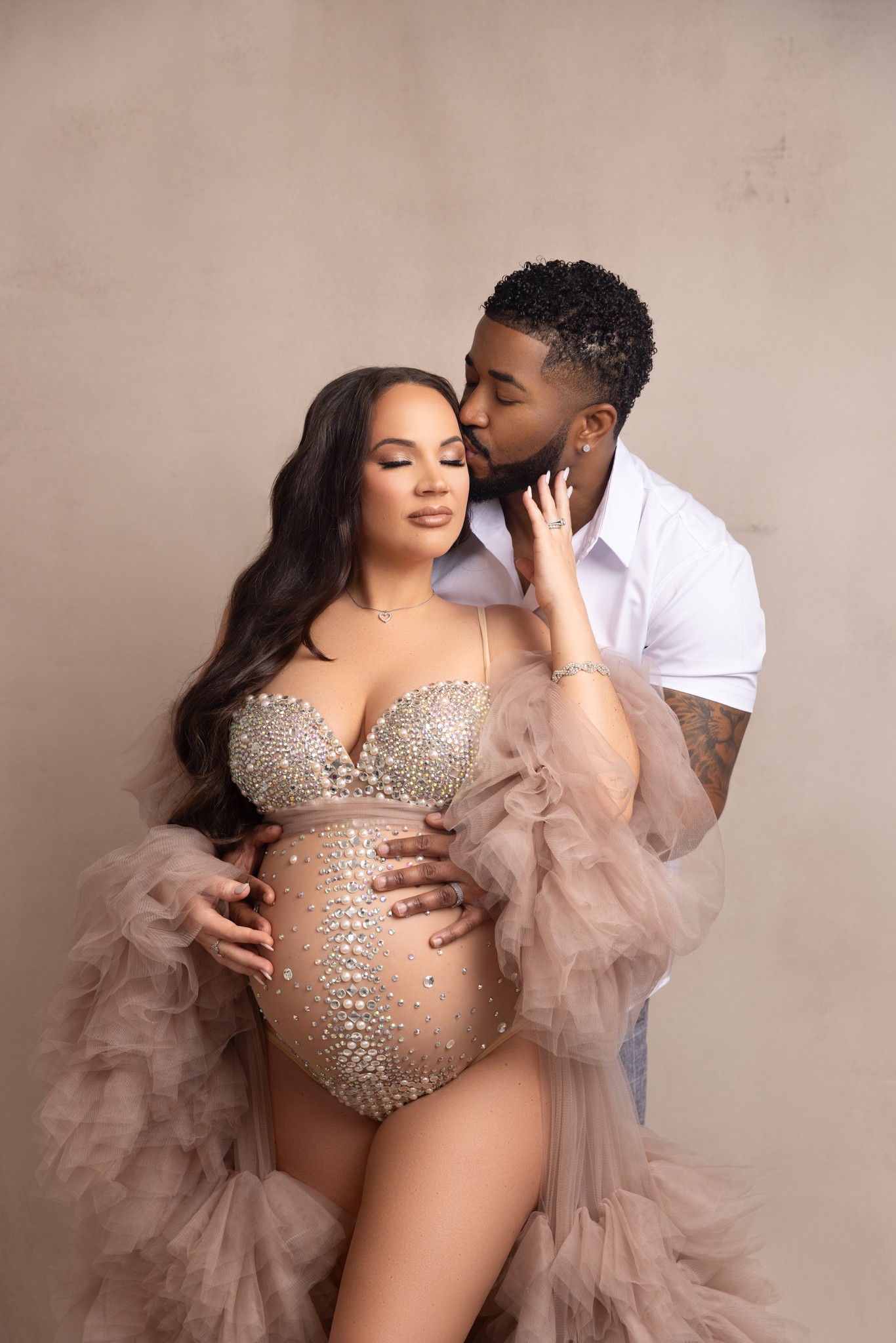 mom poses in a tulle robe and bedazzled bodysuit with dad in a loving embrace for maternity photos with a nj maternity photographer