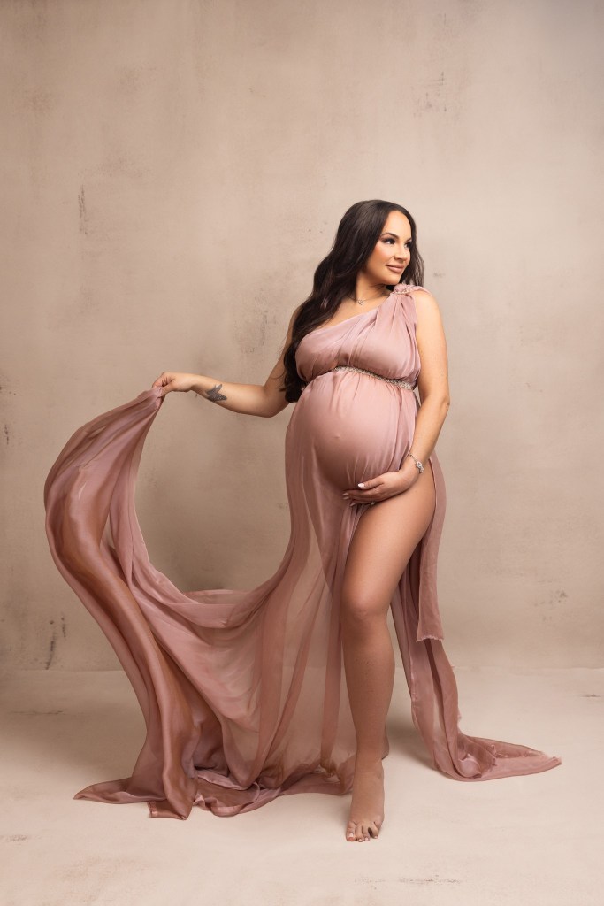 mother to be glows while wrapped in blush pink fabric for her maternity photos with a nj maternity photographer
