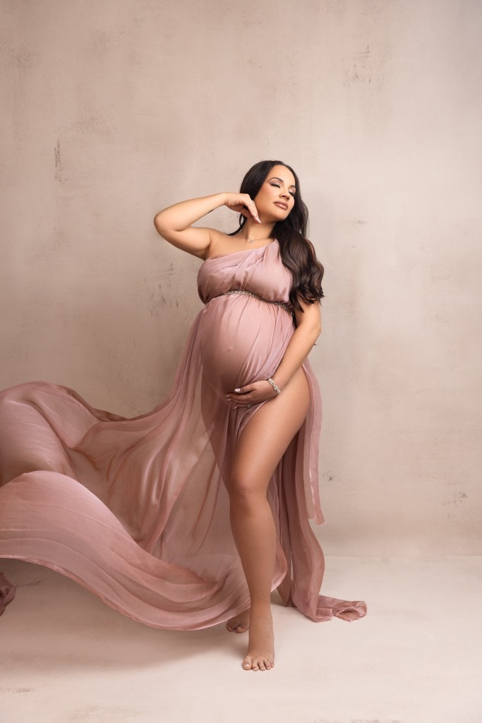 mother to be glows while wrapped in blush pink fabric for her maternity photos with a nj maternity photographer