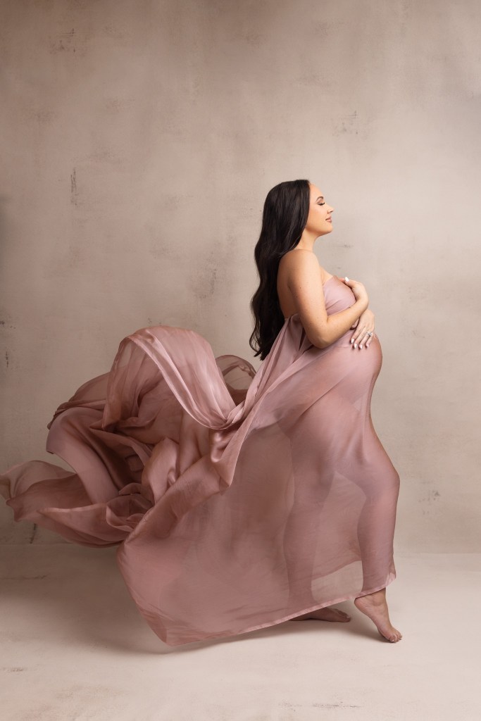 mother to be glows while wrapped in blush pink fabric for her maternity photos with a nj maternity photographer