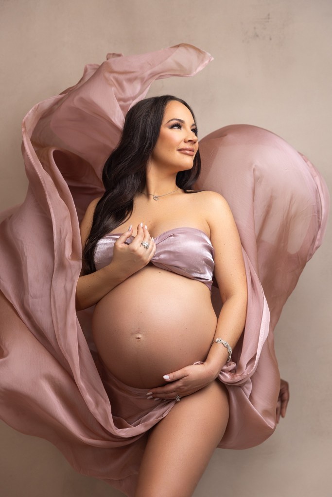 mother to be glows while wrapped in blush pink fabric for her maternity photos with a nj maternity photographer