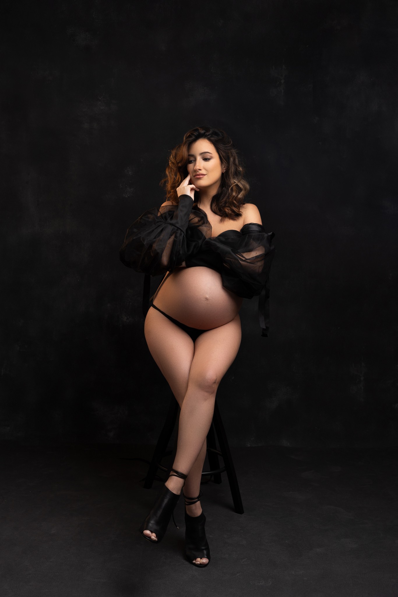 mom poses on a stool in a black outfit highlighting her baby bump during a a photo session with a nj maternity photographer