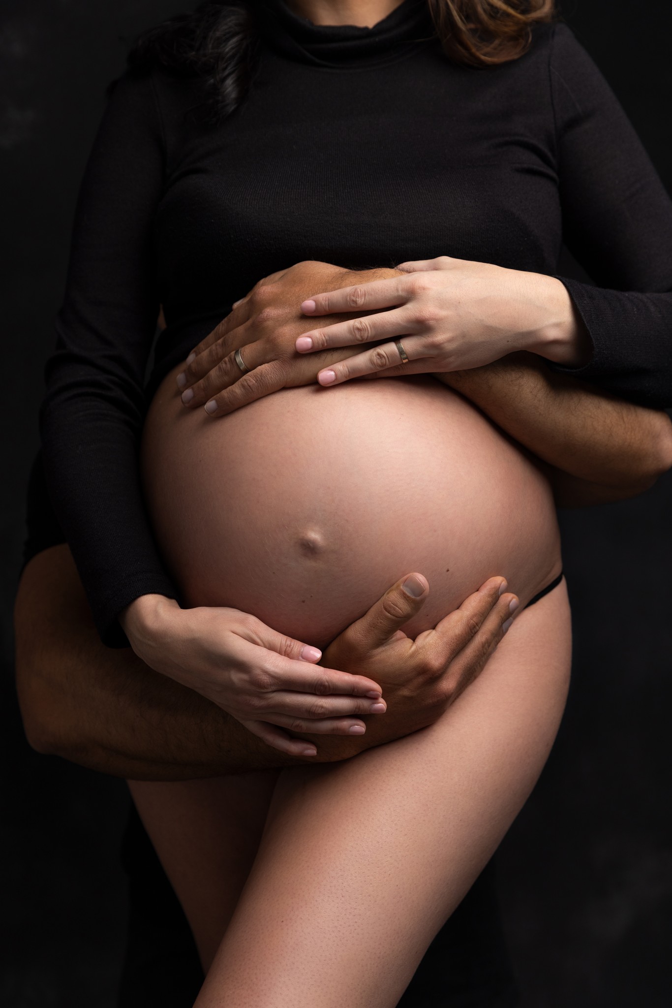 hands cradle a baby bump against a black backdrop during a nj maternity photography session