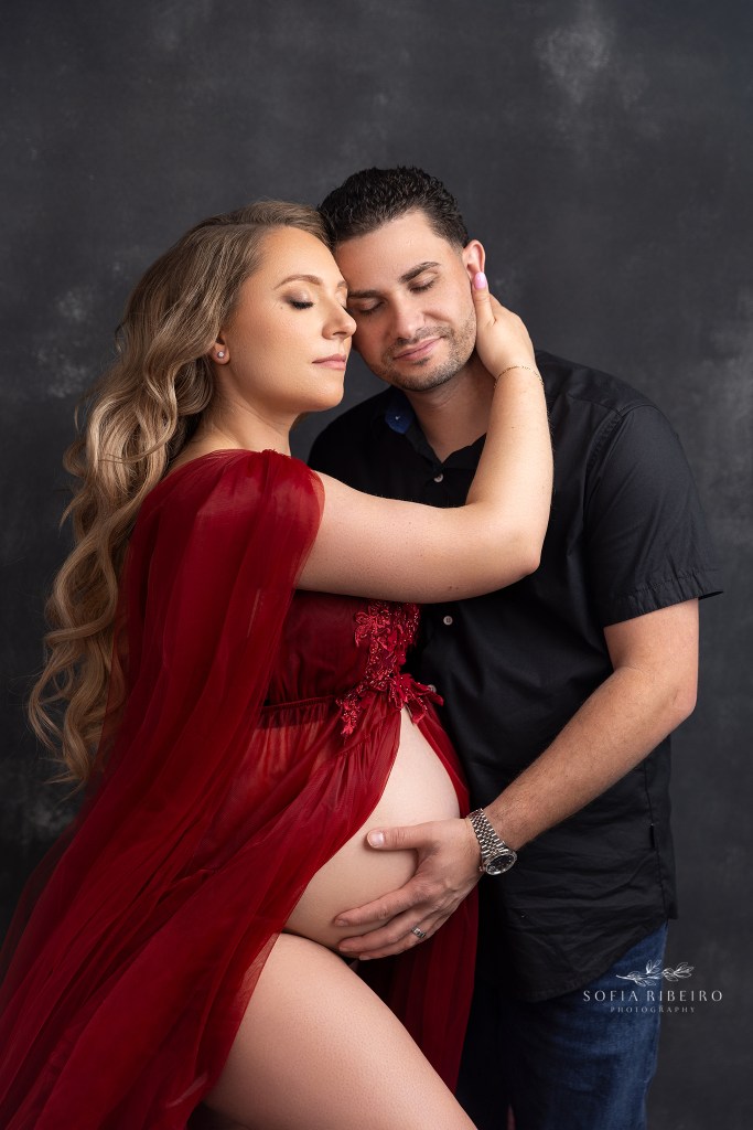 mom cradles dad's face lovingly while he places a hand on her belly