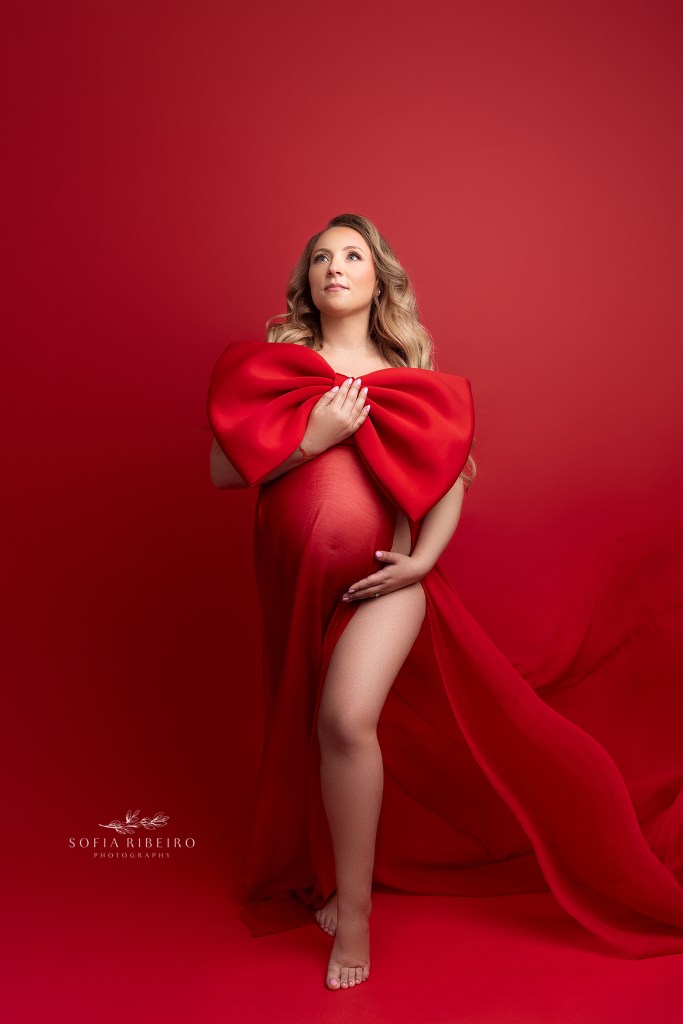 mom wears a red dress with a giant bow highlighting her bump during maternity photos