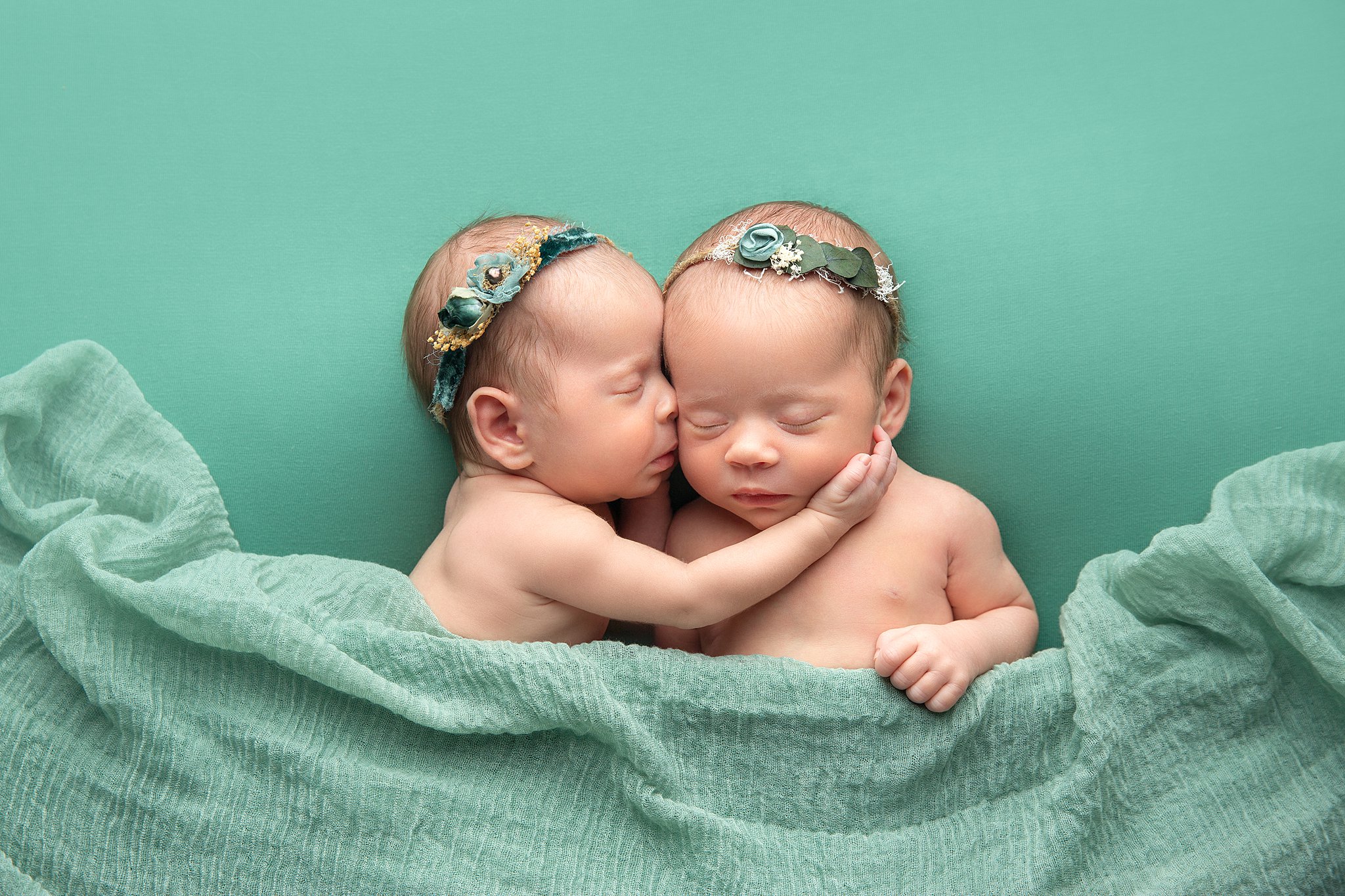 Newborn baby twins snuggle while sleeping under a green blanket