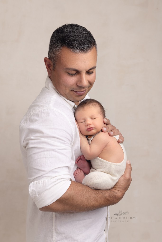 dad beams proudly at his baby boy snuggled in his arms during a photo session in red bank nj