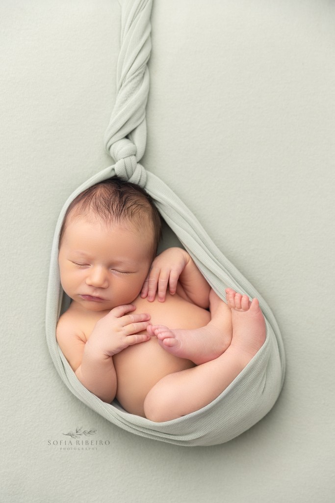 baby boy is wrapped in a sage green wrap in the womb pose during his newborn photos