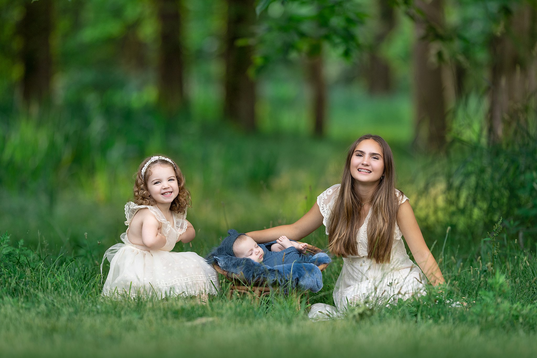 A young girl sits in a forest lawn with her newborn brother and toddler sister after meeting hoboken pediatricians